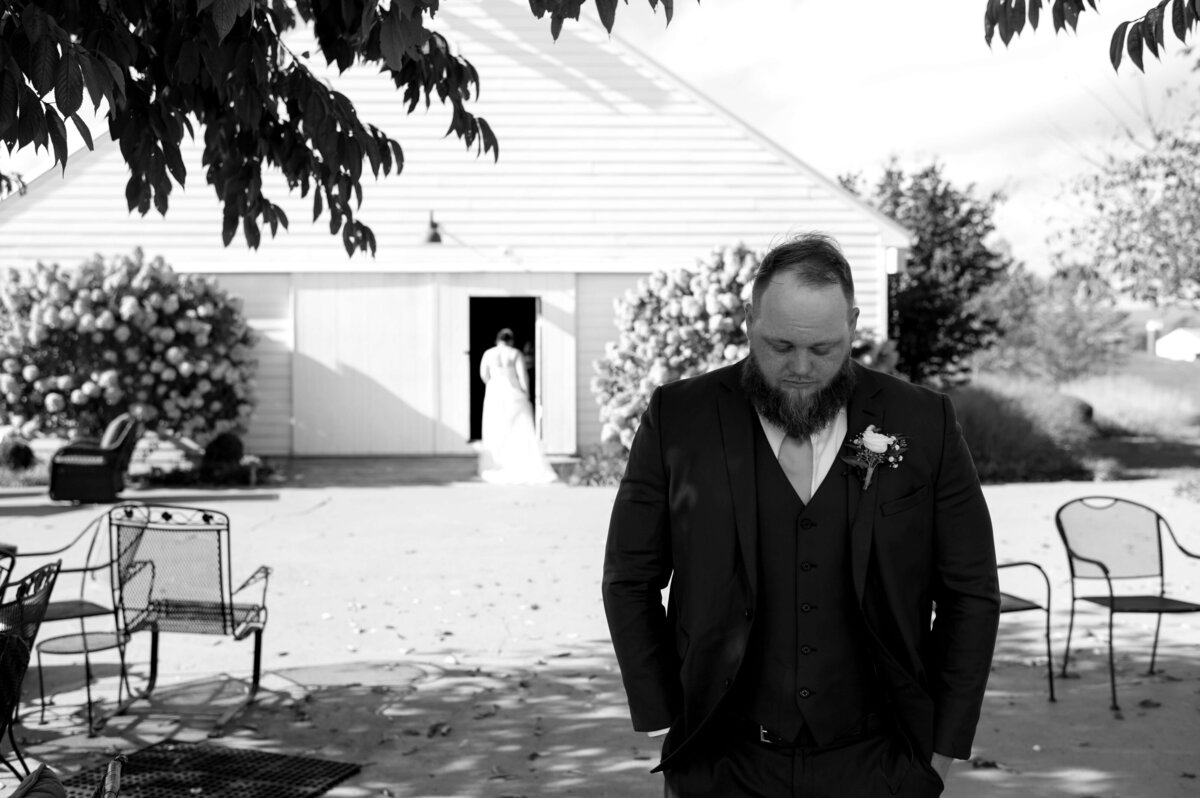 black and white wedding photo of groom standing under a tree as he waits for his bride to share a first look outside of their venue at Sunny Slope Farm