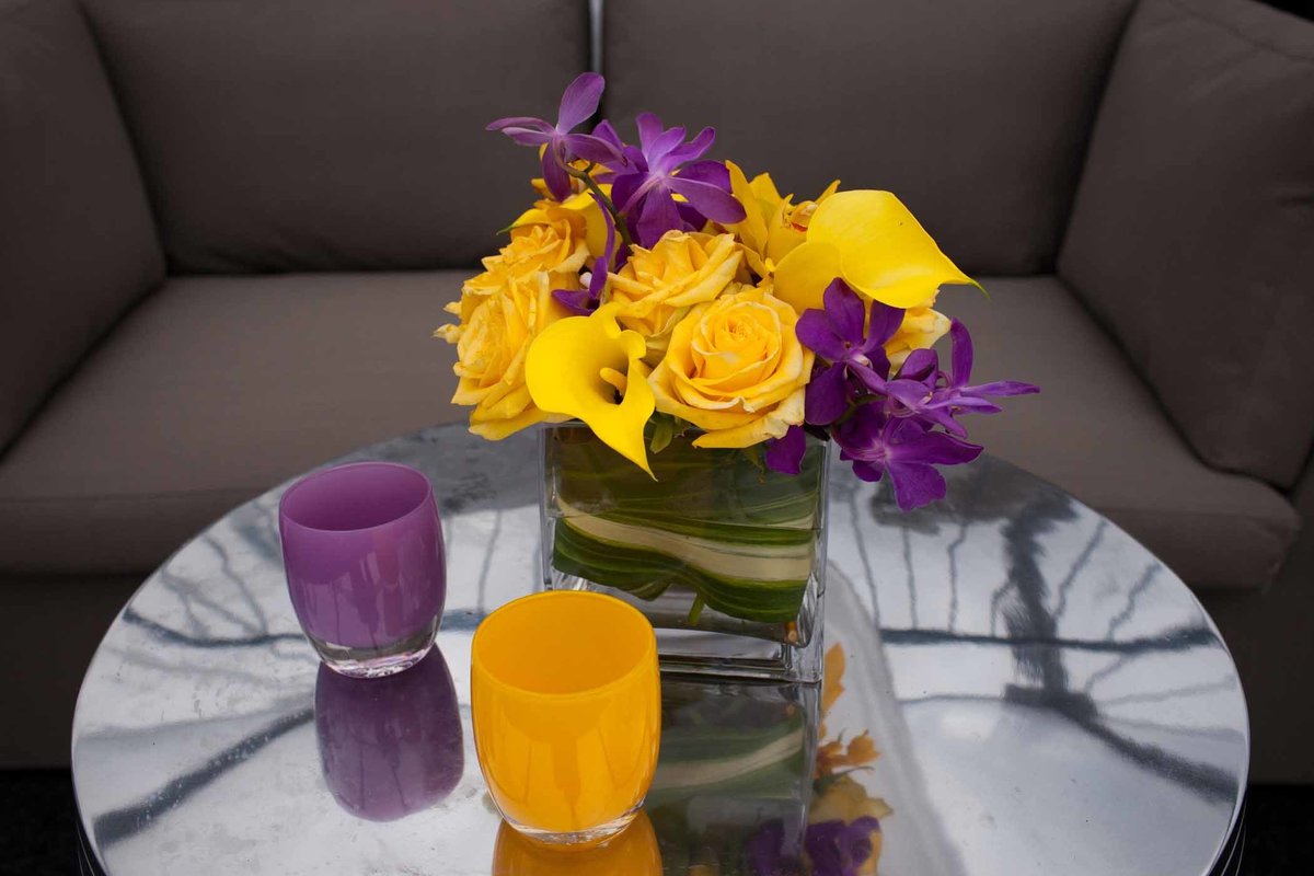 centerpiece of yellow roses, purple orchids, and yellow callas on cocktail table