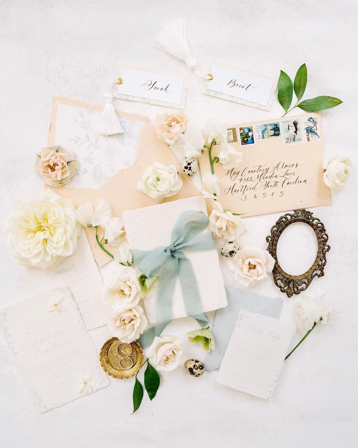 Newport Wedding Photographer | Delicate flat lay with vintage envelopes, white flowers, a blue-ribboned gift box, and a small ornate frame on a white background.