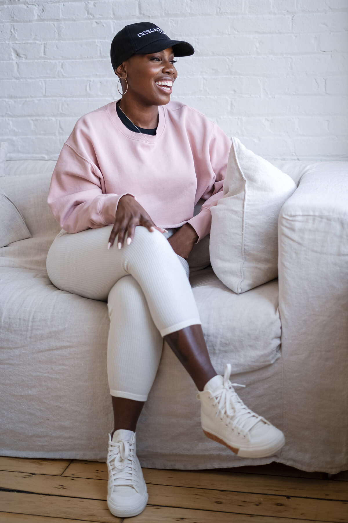 A candid moment of the artist laughing, seated comfortably on a linen couch in a sunlit studio. The image captures the ease and joy she brings to her work, framed by clean textures and warm light.