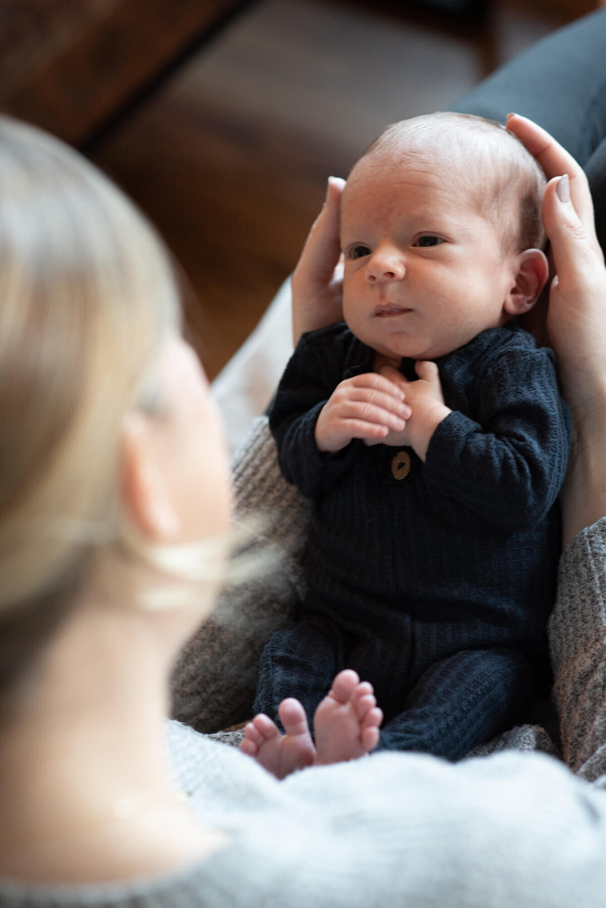 An image captured by a Denver Newborn Photographer of a newborn baby laying in mom's hands and looking back up at her