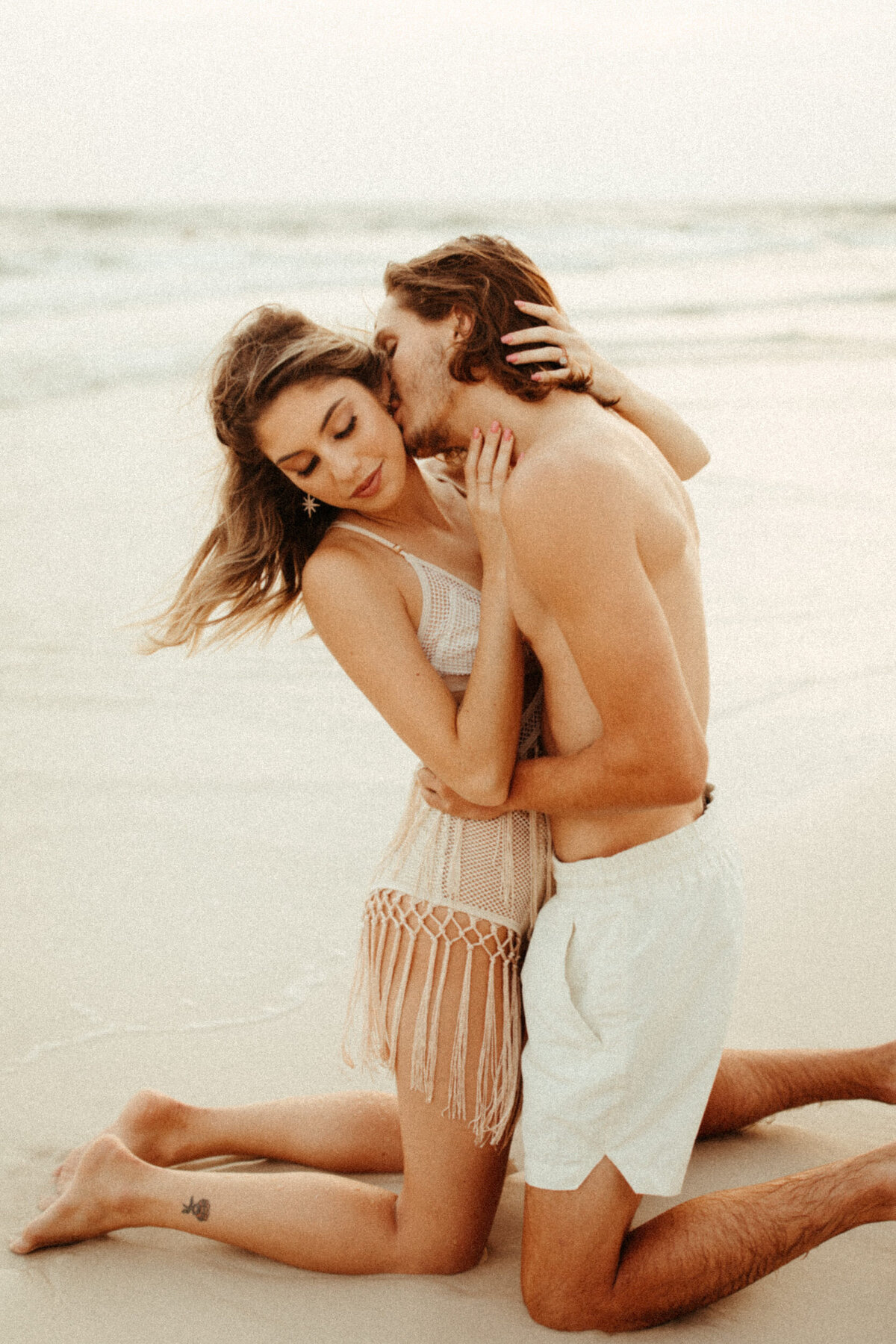 Girl in boho fringe swimsuit with her fiance kissing her at the beach