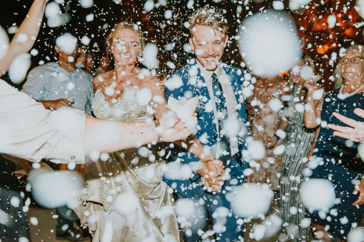 Confetti is thrown in front of camera as bride and groom exit wedding together.