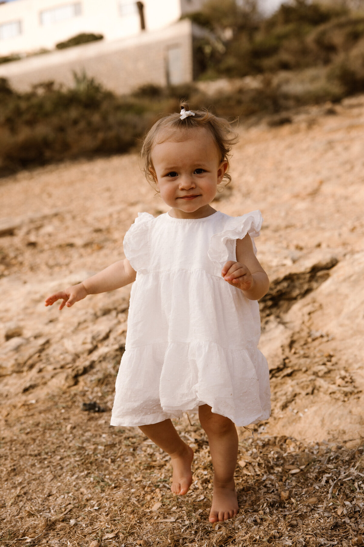 A little girl in a dress is walking on rocks towards the photographer during a family photoshoot on Ibiza