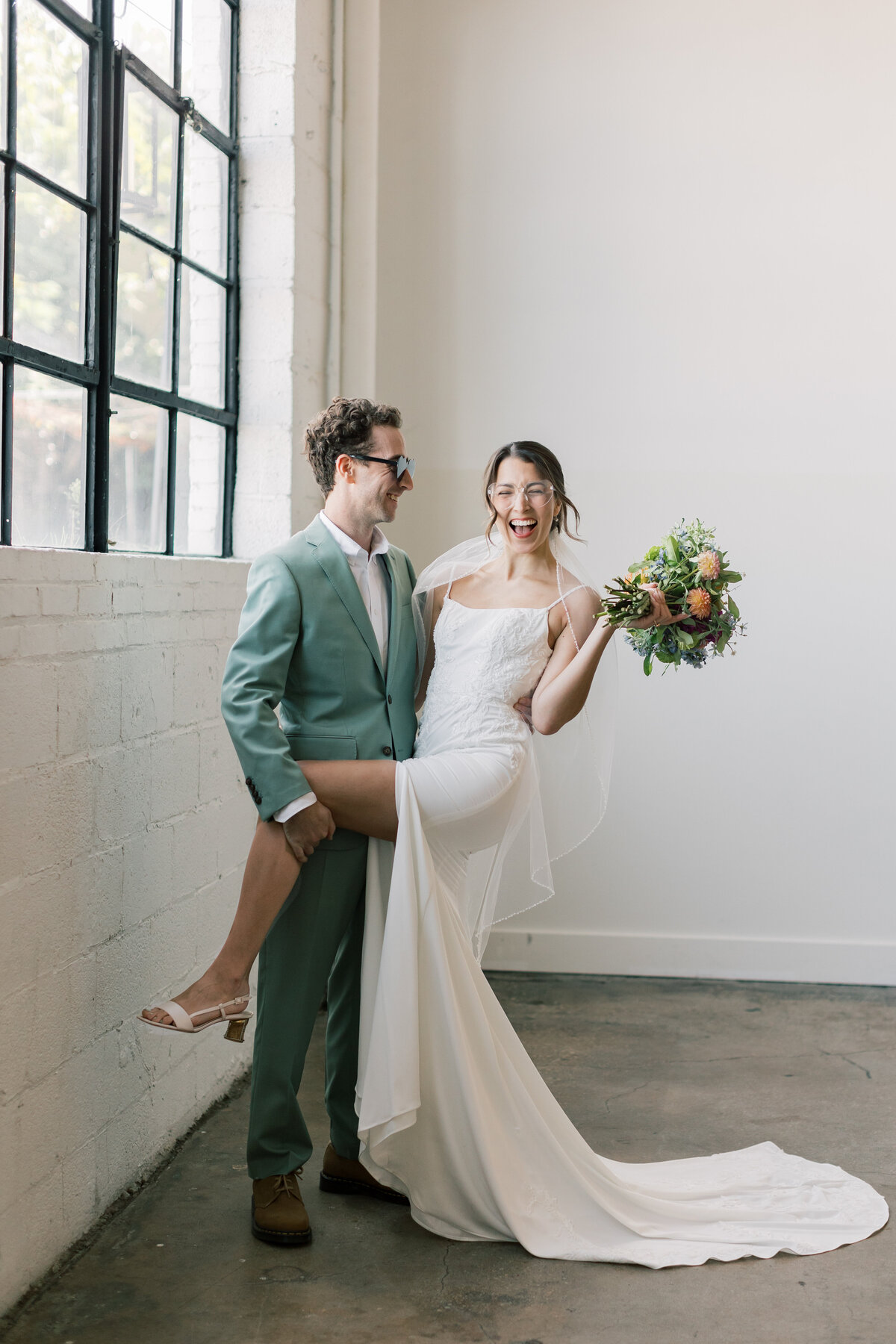 Sara holding vibrant bouquet by Crimson & Clover standing beside Brendan in modern indoor portrait at Fetewell wedding.