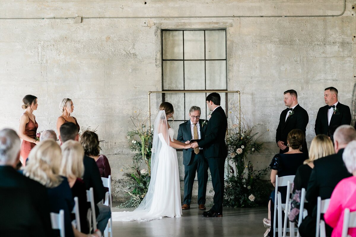 Bride and groom holding hands during the ceremony as their guest look on at Olde Dobbin Station