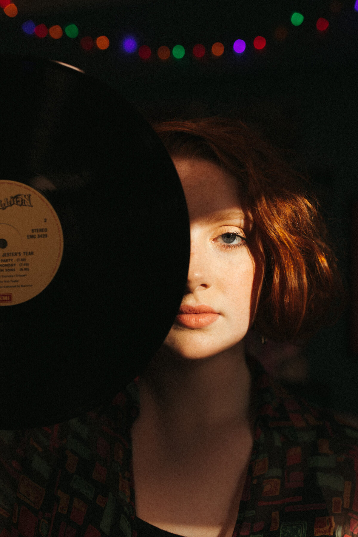High school senior girl in record store holding vinyl over half of her face