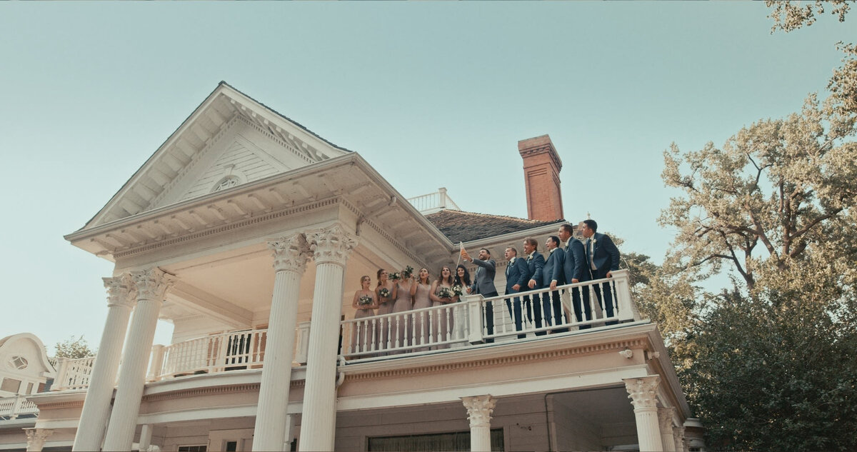 Wedding party standing on balcony of The Norland Historic Estate, captured by Prairie Orchid Weddings, wedding videographers in Lethbridge, Alberta. Featured on the Bronte Bride Vendor Guide.