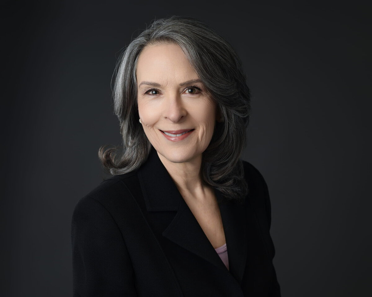 Executive woman in dark blazer with confident smile, captured by a Toronto headshot photographer in studio lighting.