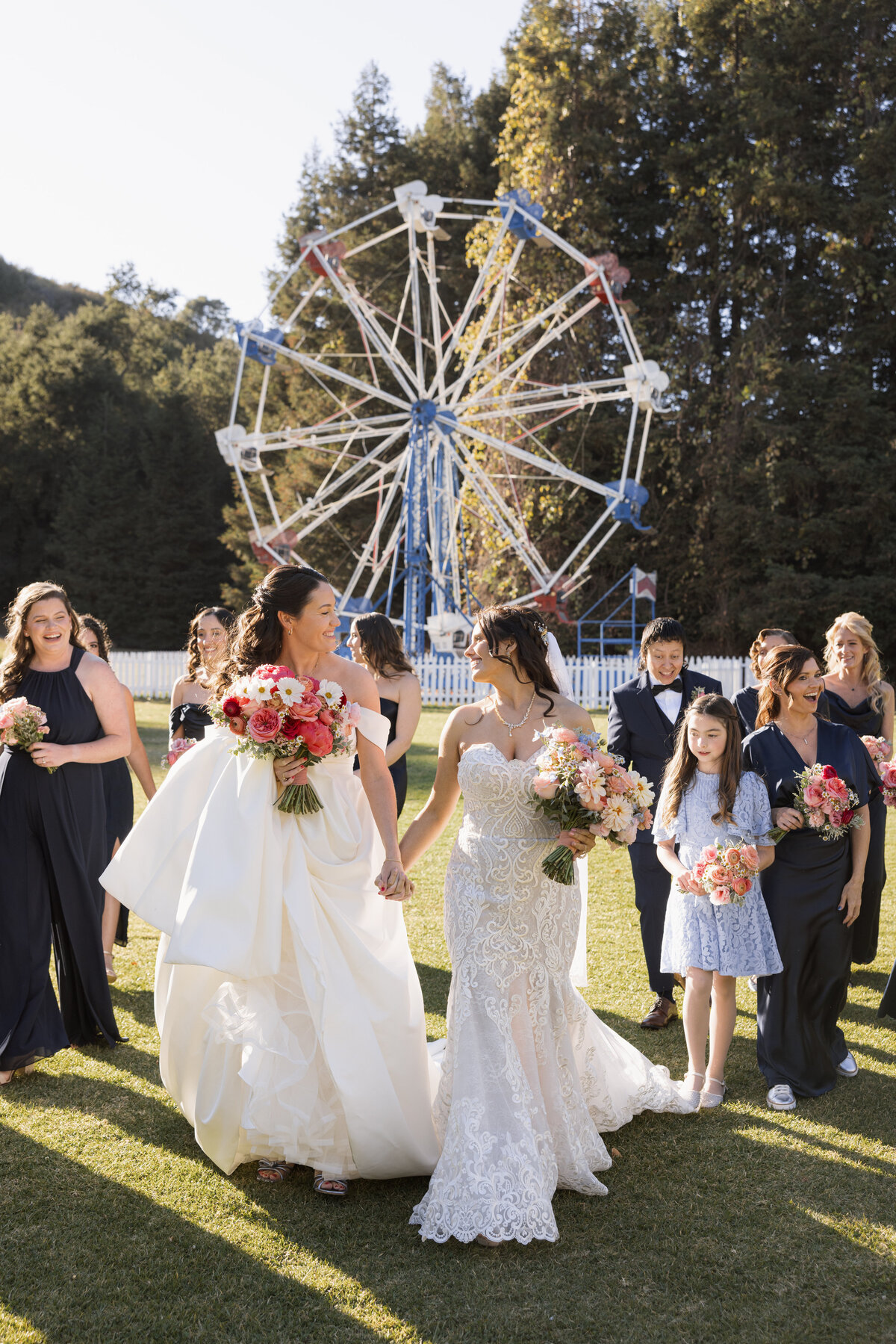 Queer couple with bridesmaids in navy blue dressed in front of Ferris Wheel at Calamigos Ranch