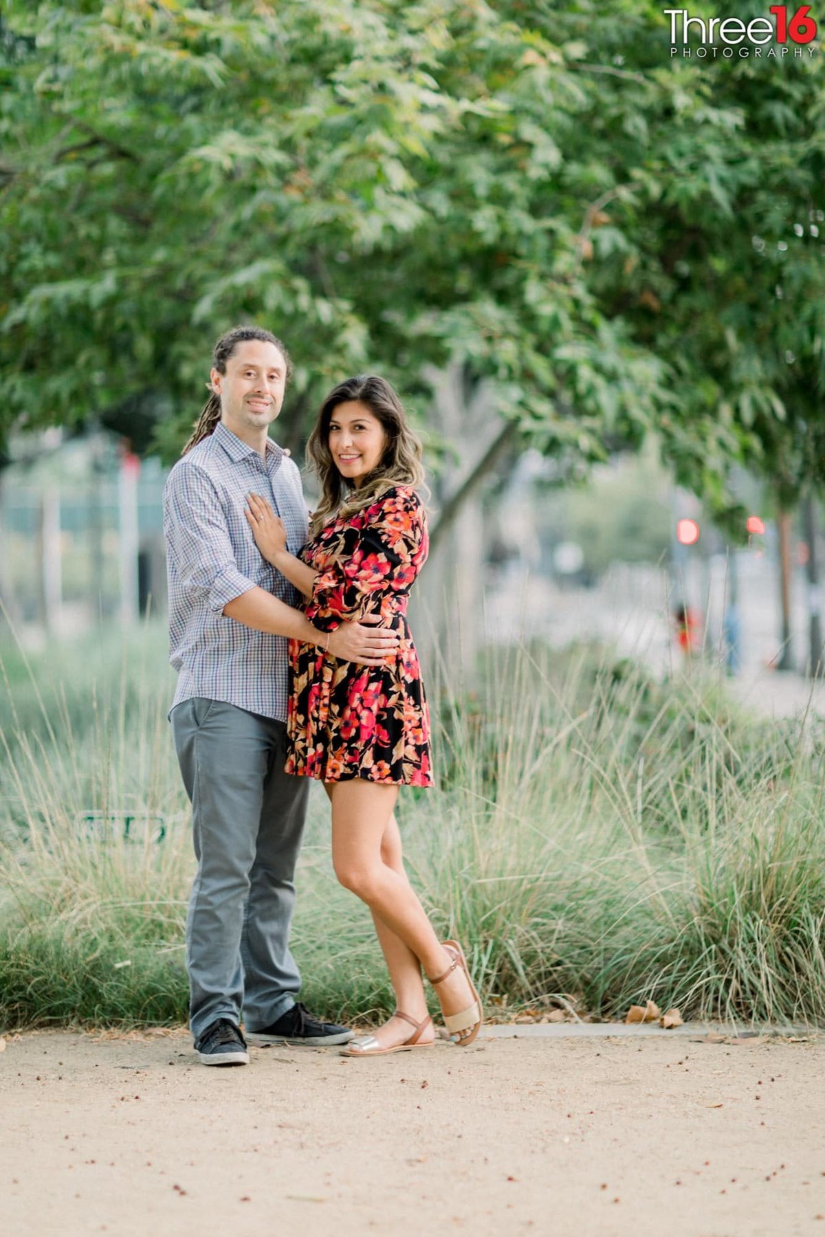 Engaged couple pose together in front of tall grass at the LA City Hall
