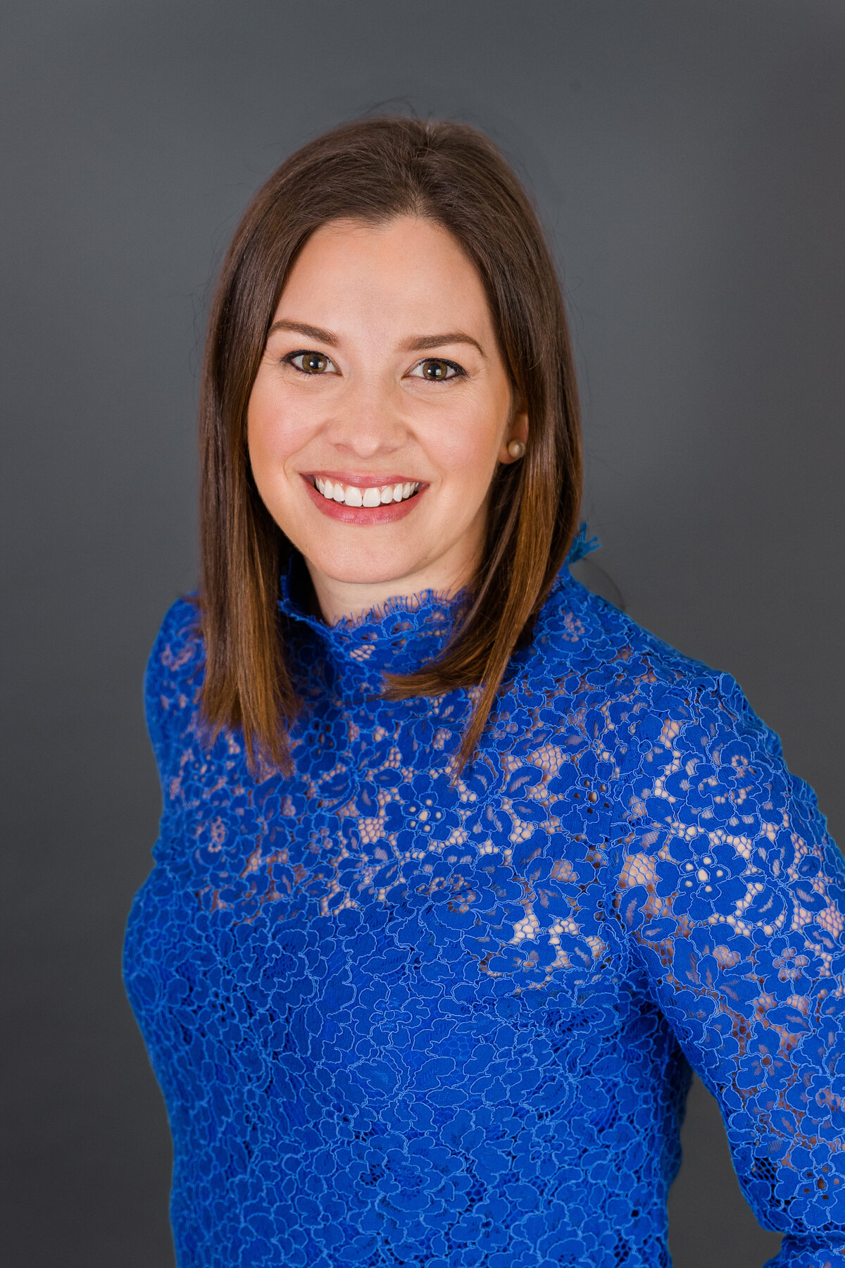 woman in bright blue textured dress stnading sideway to the camera in front of a gray backdrop during portrait session