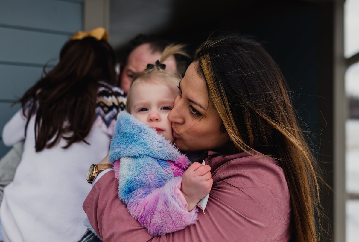 Mom holds young daughter and gives her a kiss.