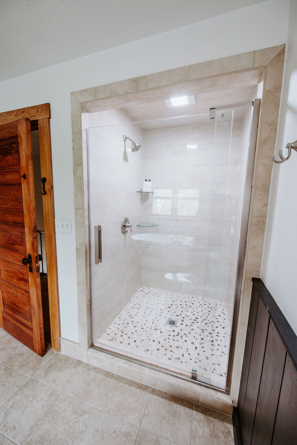 travertine shower with tumbled stone shower floor tile and black wainscotting in the second floor bathroom of the modern farmhouse overnight accommodation at Willowbrook wedding venue