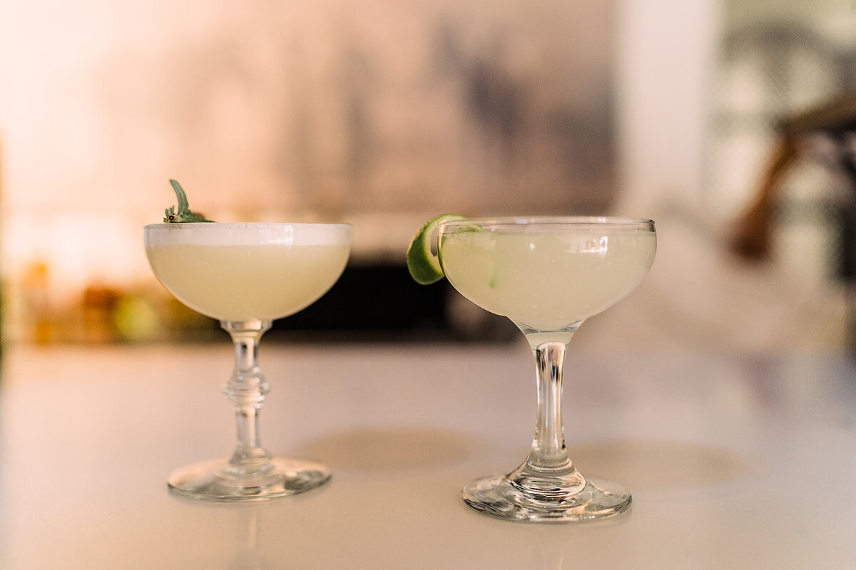 Close-up of two elegant cocktails garnished with herbs and lime, sitting on a white countertop ready for a celebration.