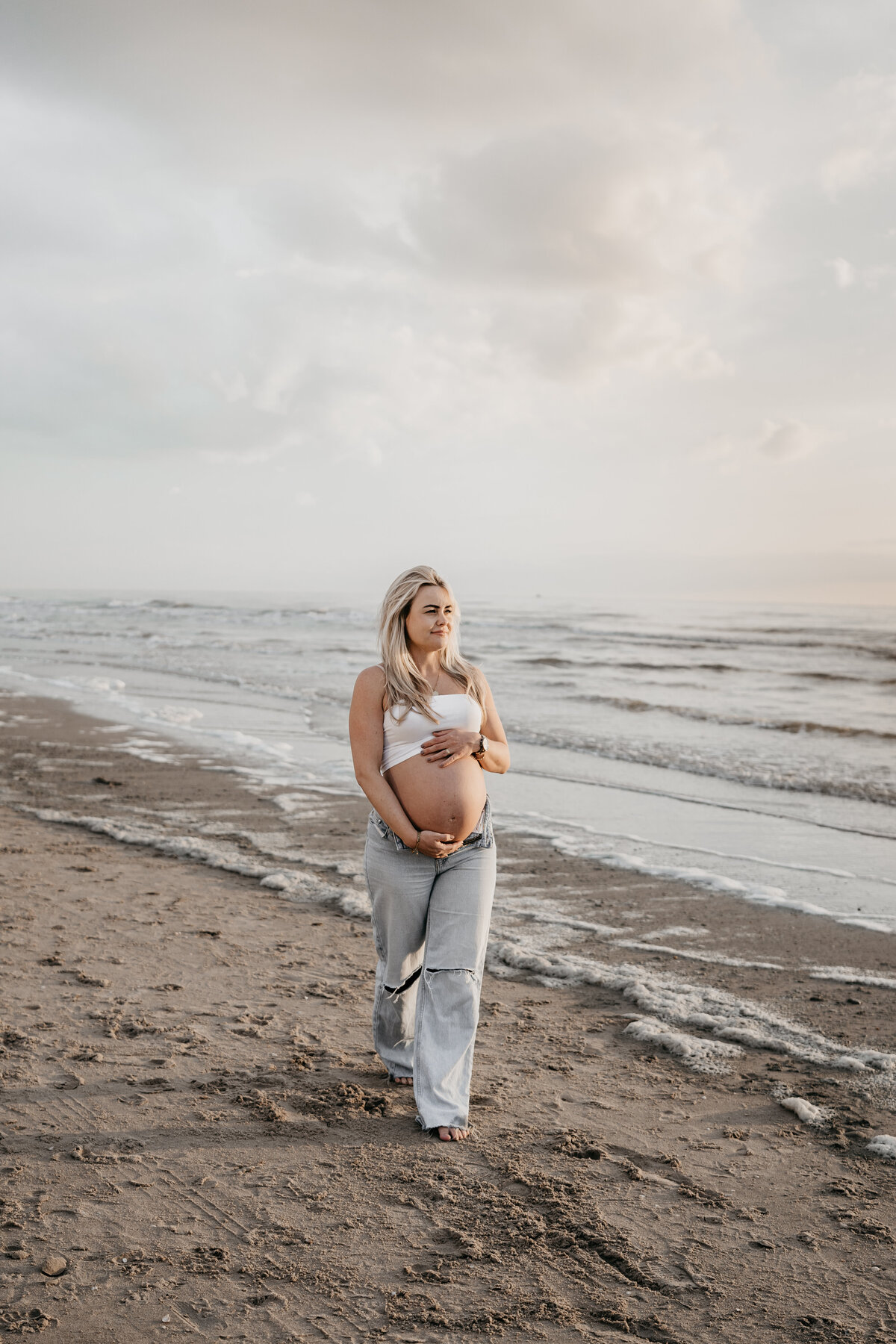 Zwangere vrouw aan het strand tijdens zonsondergang.