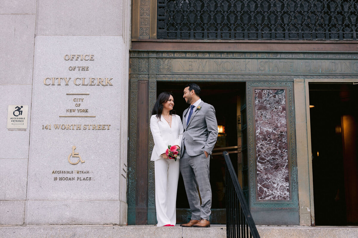 The bride and the groom are happily staring at each other in front of the NYC Office of the City Clerk. Image by Jenny Fu Studio