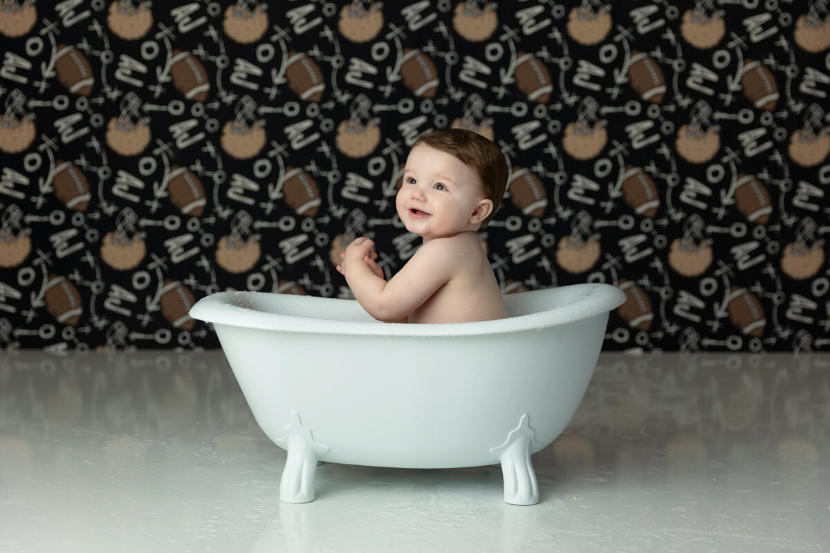 A toddler boy cleans up in a tub in a football themed studio