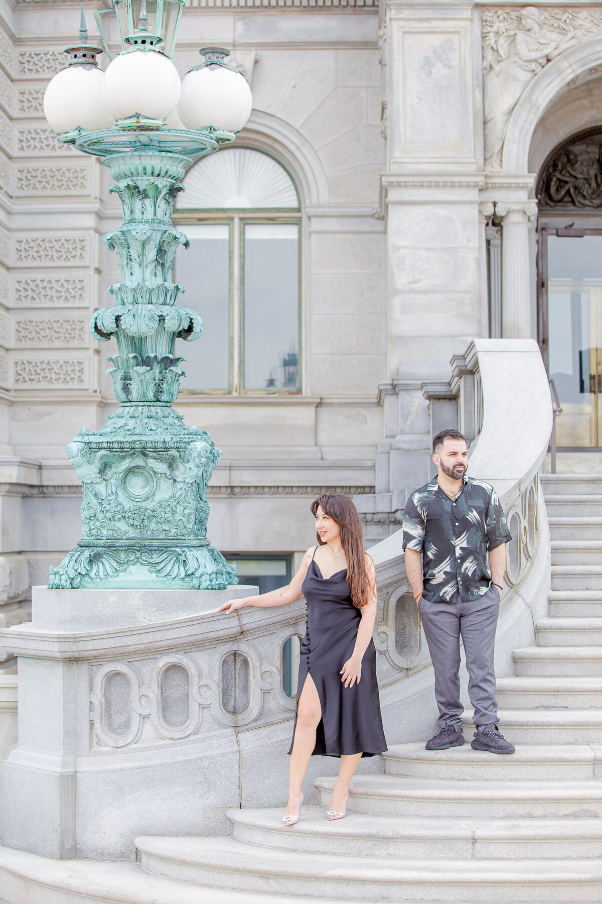 A couples stands next to beautiful architecture in downtown D.C. They are standing on stairs, posed and looking off to the side.