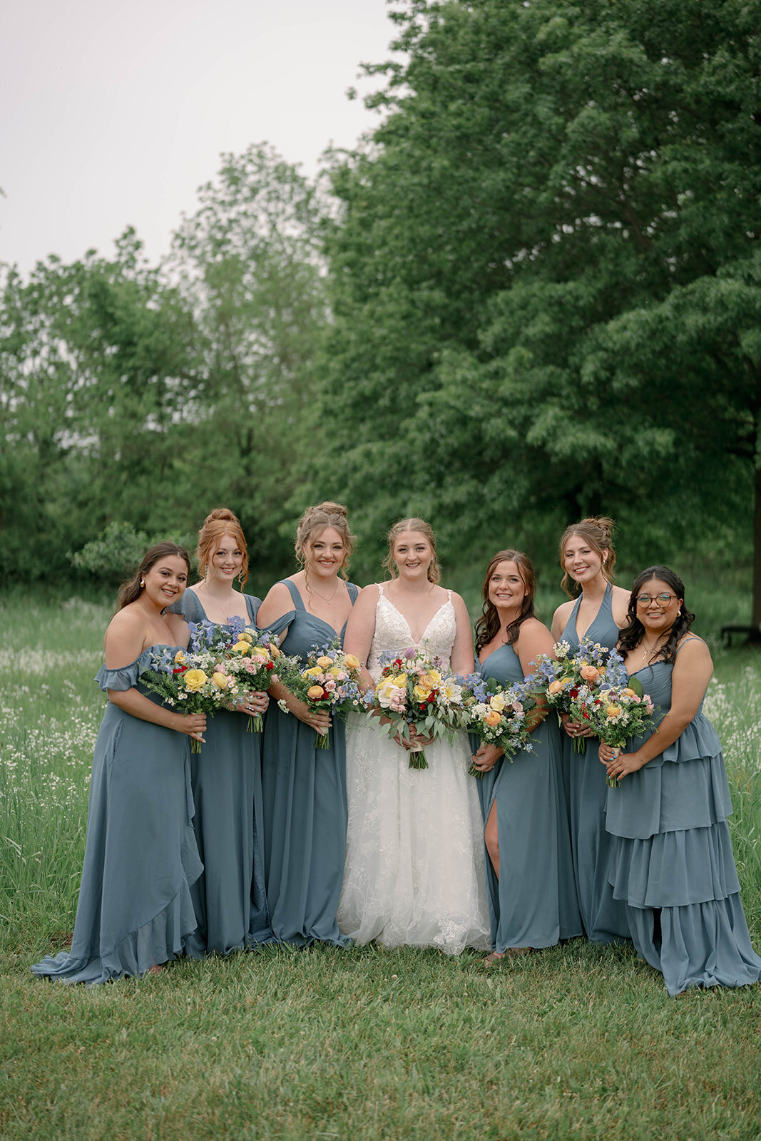 Wedding party photo of bridesmaids in matching blue dresses smiling at the camera during a Blue Heron Barn wedding in Kalamazoo MI.