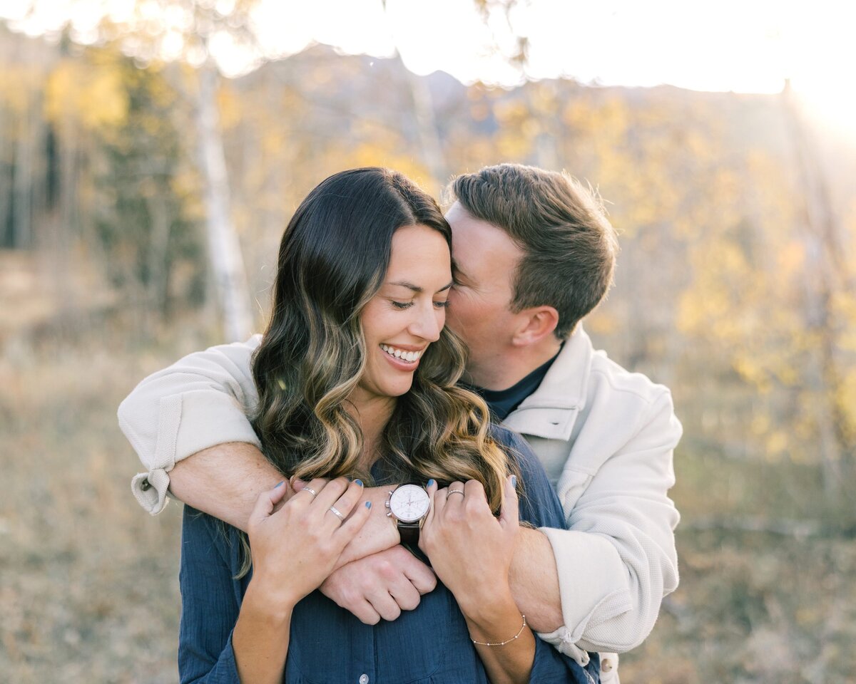 This is a close up of the young couple. The man has his arms wrapped around his girlfriend, nuzzling into her ear. 