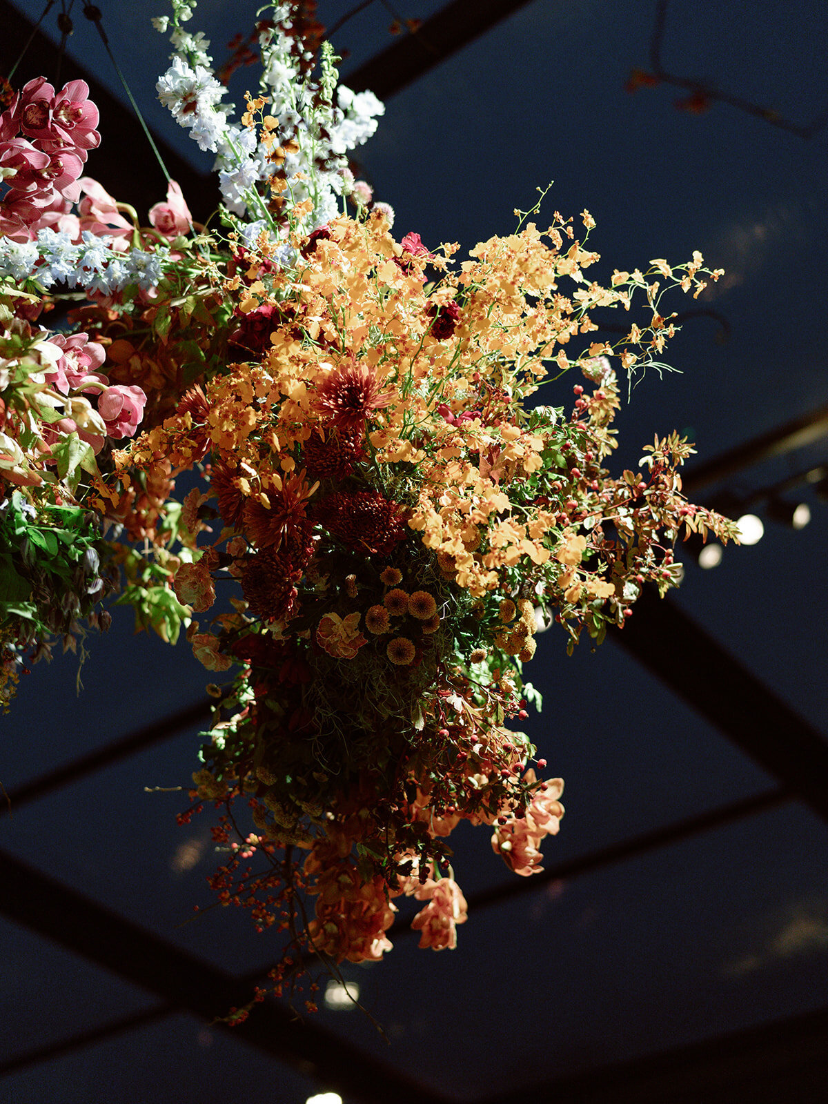 Interacting and sculptural floral clouds hang over the dance floor and bars of this fall wedding reception in Tennessee. Clear top tent build out for fall wedding reception in Tennessee hills.  Product clustered floral clouds in a tasteful fall color palette of copper, ruby, gold, burgundy, rust, and lavender. Orchids, bittersweet berries, butterfly ranunculus, and tulips are highlighted. Unique floral design with flower forward large scale installations. Design by Rosemary & Finch Floral Design in Nashville, TN.