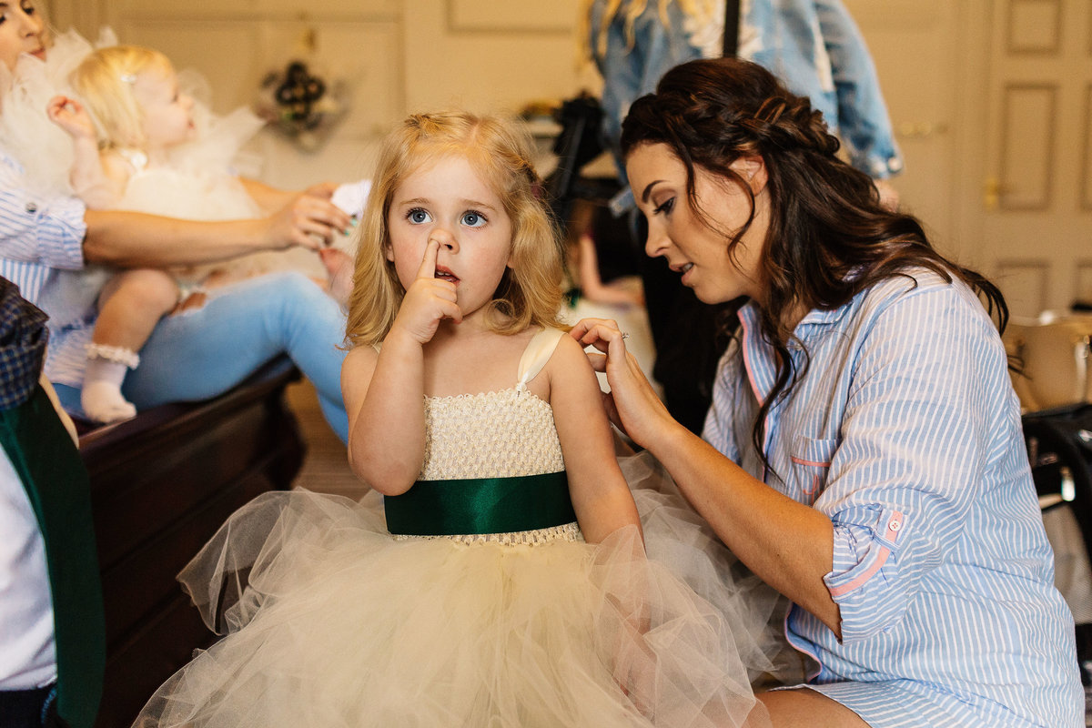 Informal photo of a Flower girl picking her nose as the bride dresses her