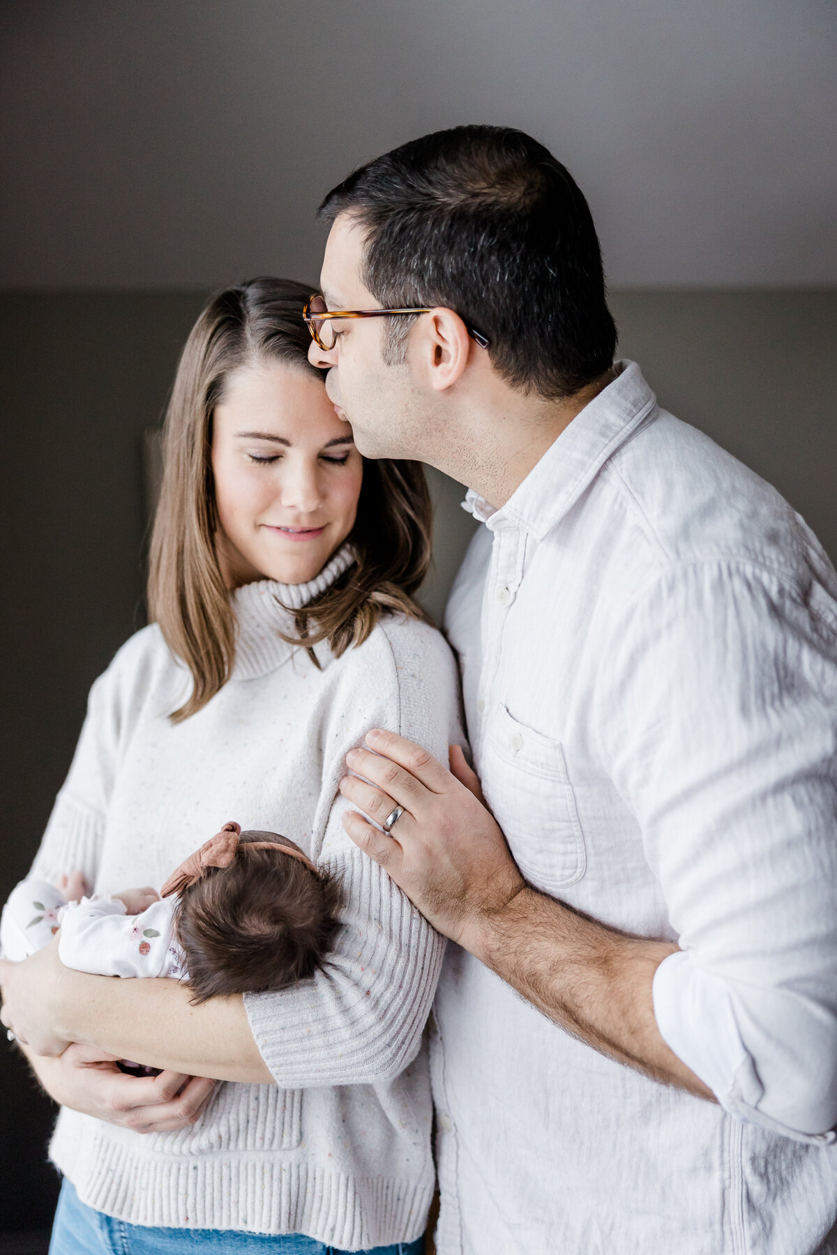 husband kissing his wife holding newborn baby