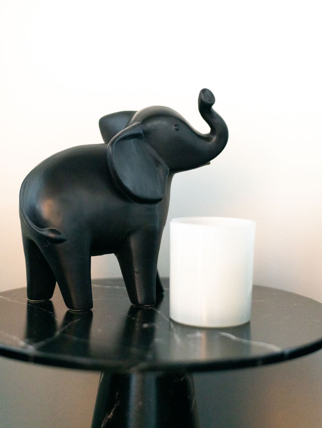 a black elephant statue and white candle on a black side table