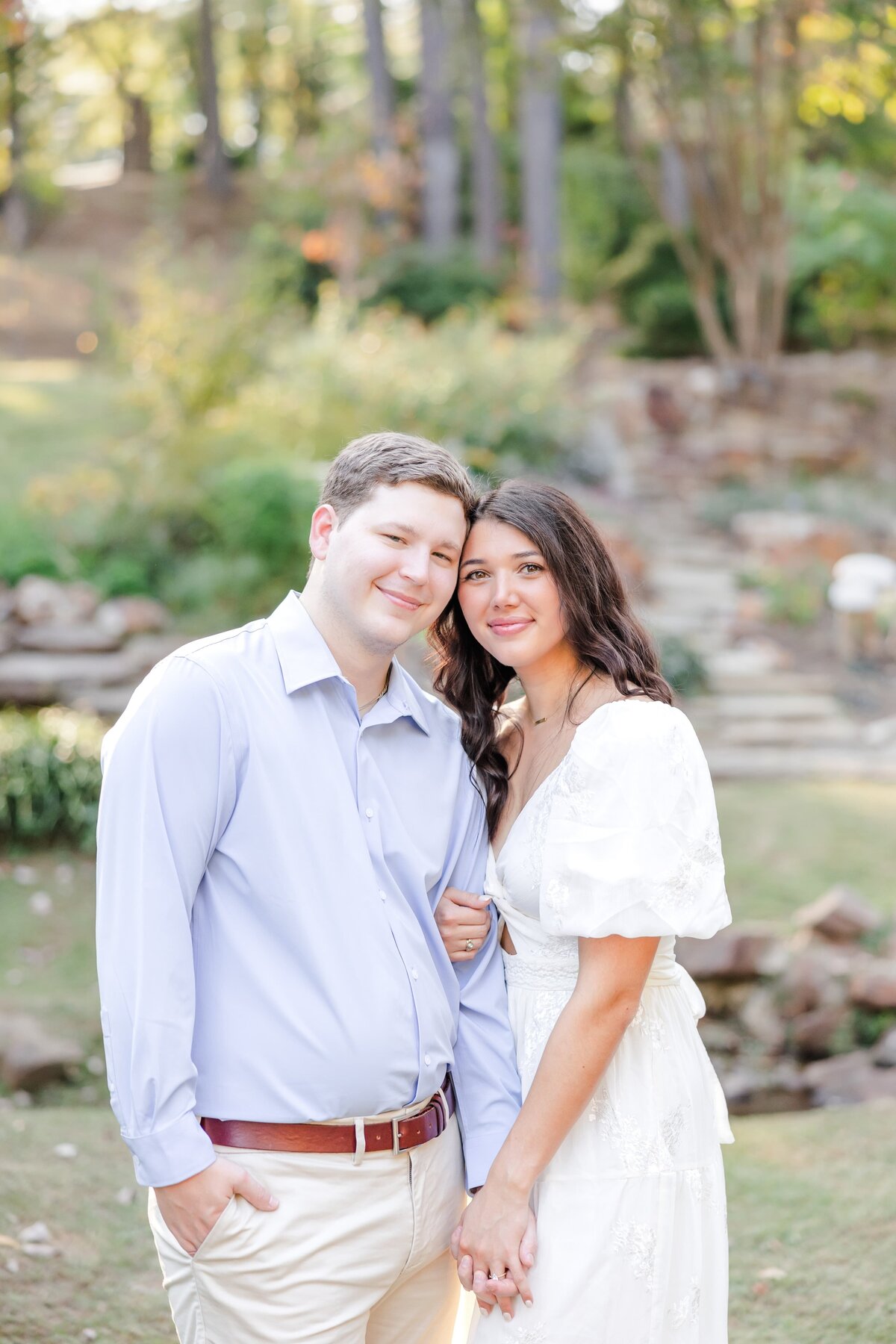 A woman in a white dress snuggles on her fiancee in a garden