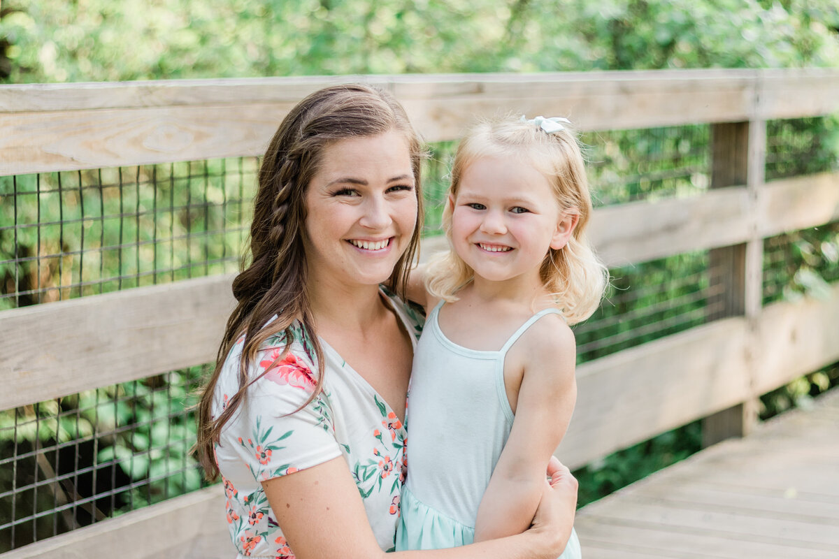 mom and young daughter on a bridge hugging and smiling