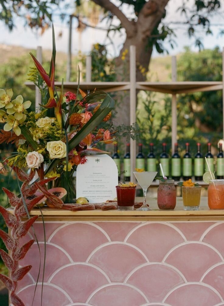 Pink scalloped bar with tropical florals and vibrant drinks, cocktail hour inspiration for a colorful Airlie Gardens wedding