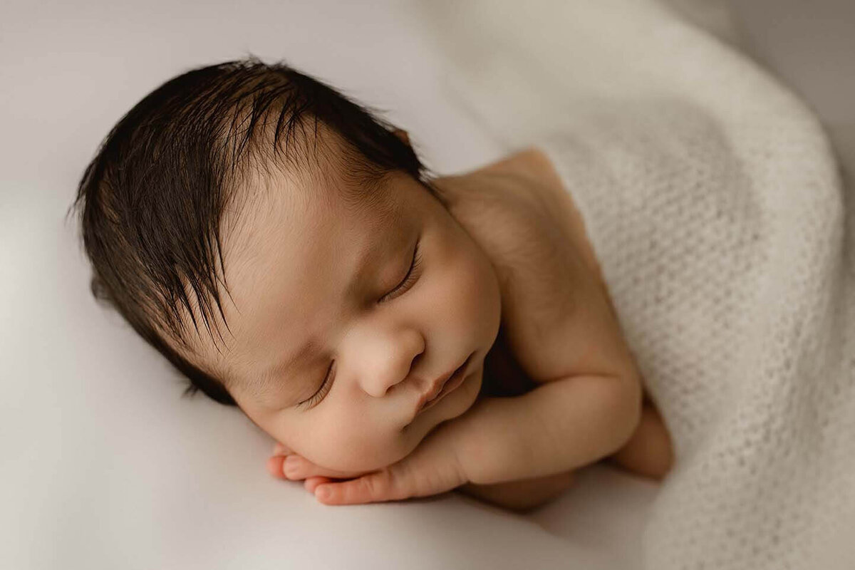 A newborn boy sleeping with his hand under his cheek with a blanket draped over him