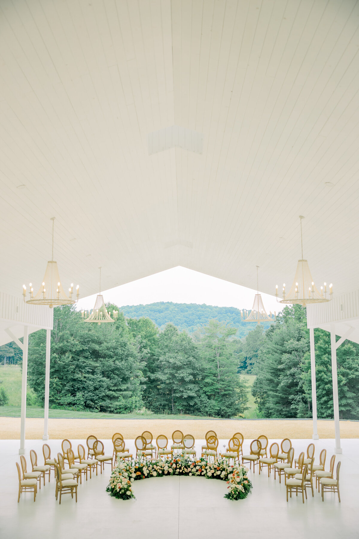 Ivy Rose Barn | A ceremony site in the pavilion of the Ivy Rose Barn in Virginia. The pavilion is all white with chandeliers and features a stunning floral ground arch installation. Captured by Virginia Wedding Photographer, Caitlin Wilcox