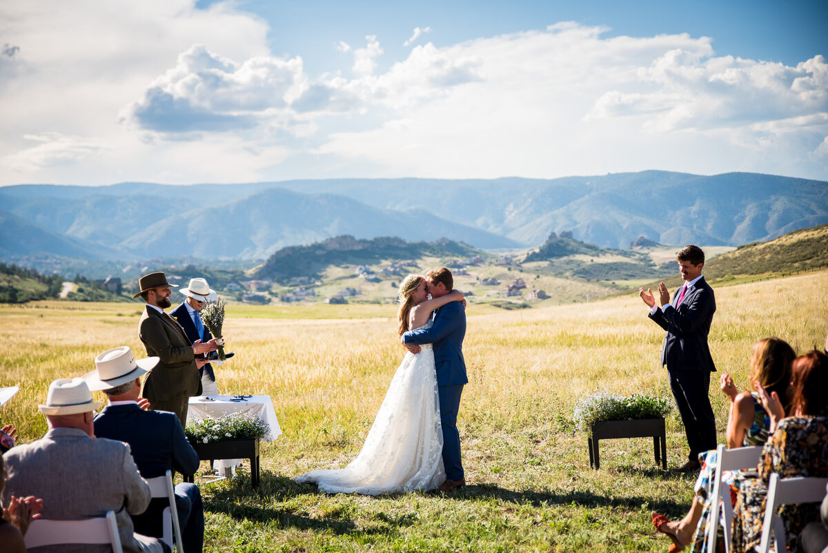 A wide angle shot of a bride and groom sharing their first kiss at the end of the ceremony with the Colorado landscape in the background.