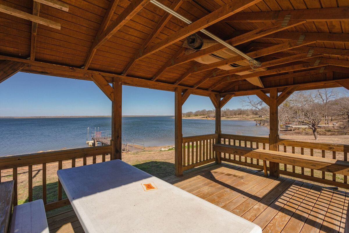 Covered outdoor patio with picnic table and plenty of seating at this 2-bedroom, 2-bathroom lakeside vacation rental home for 6 guests on Tradinghouse Lake with privacy access to a fishing dock and boat launch pad, ping pong table, gazebo, free wifi and free parking in Waco, TX.