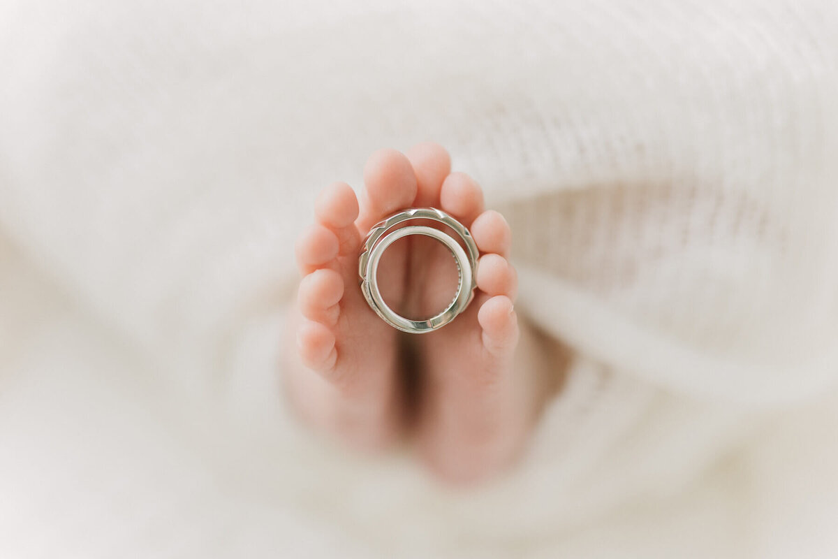 新生児の赤ちゃんの足の間にパパとママの結婚指輪がおかれている美しいニューボーンフォト