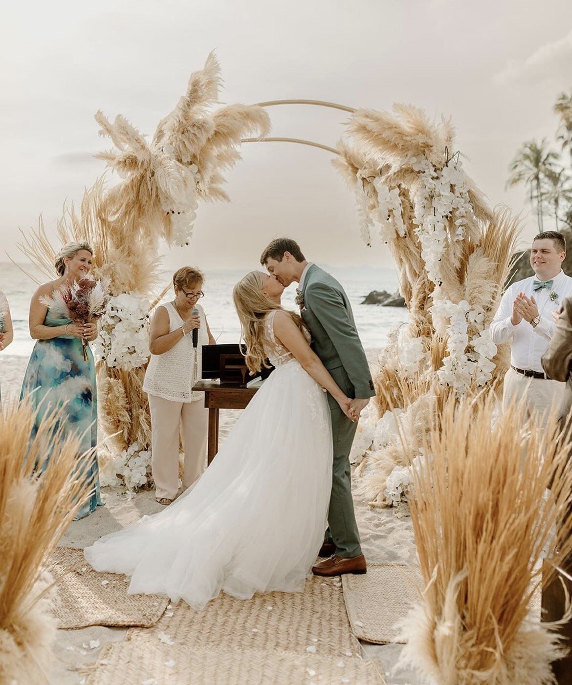 Newlyweds share a romantic first kiss at a tropical destination wedding, styled by a Mobile Makeup Artist near me specializing in mobile wedding hair and makeup.