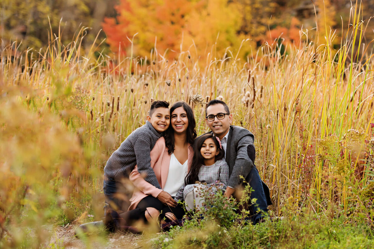 mom and dad sitting on the ground with their son and daughter in the fall foliage for their fall family photography session in Burlington, Ontario
