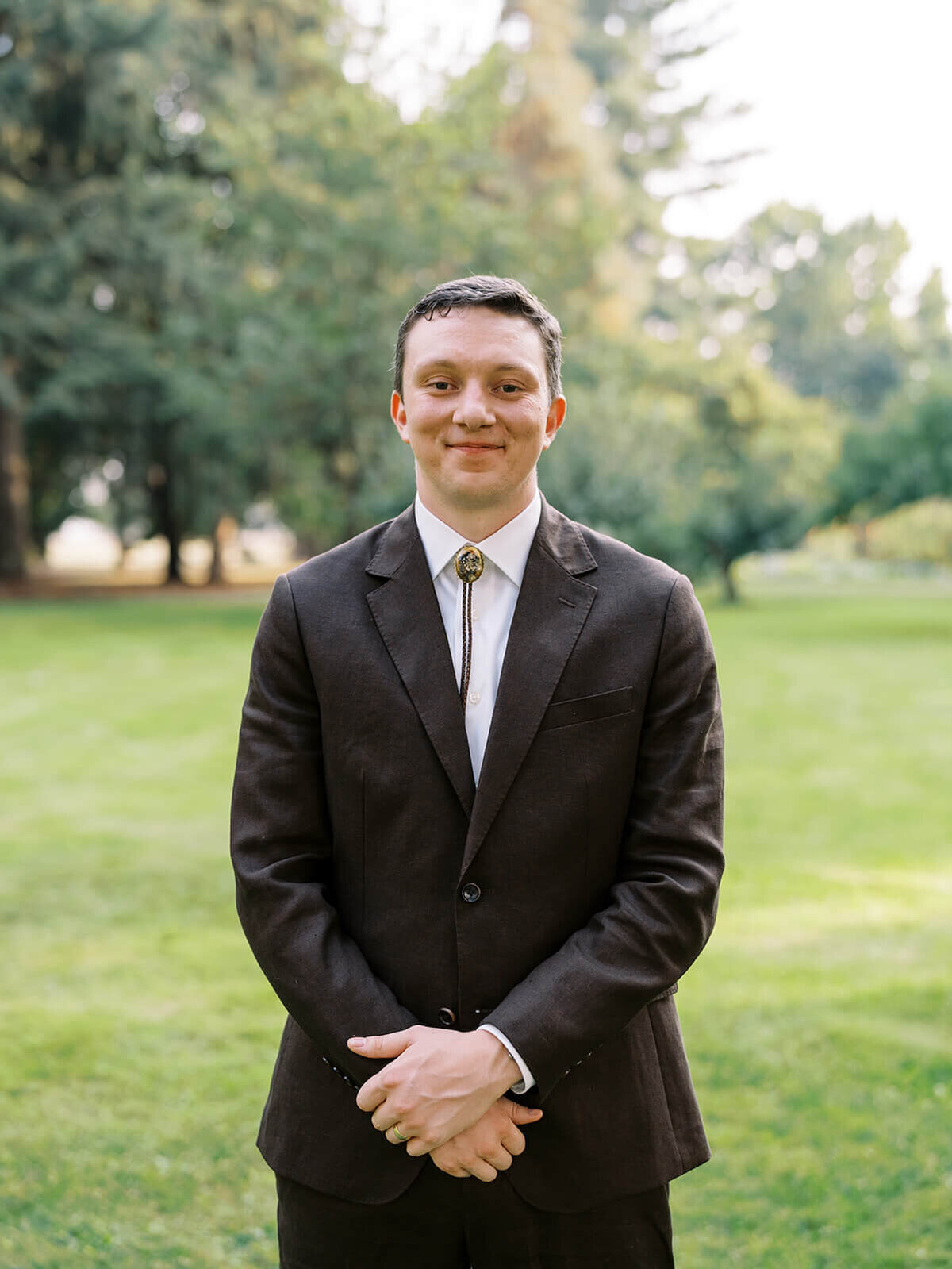 A groom smiling on his wedding day wearing a suit and bolo tie. 