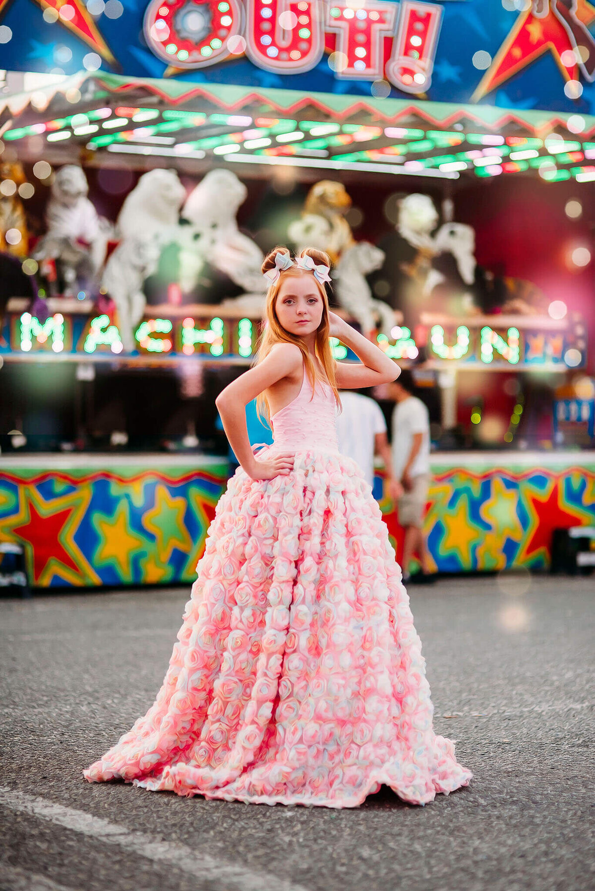red haired girl with hand on her hip in a pink rainbow dress in front of a carnival game near Annapolis Maryland