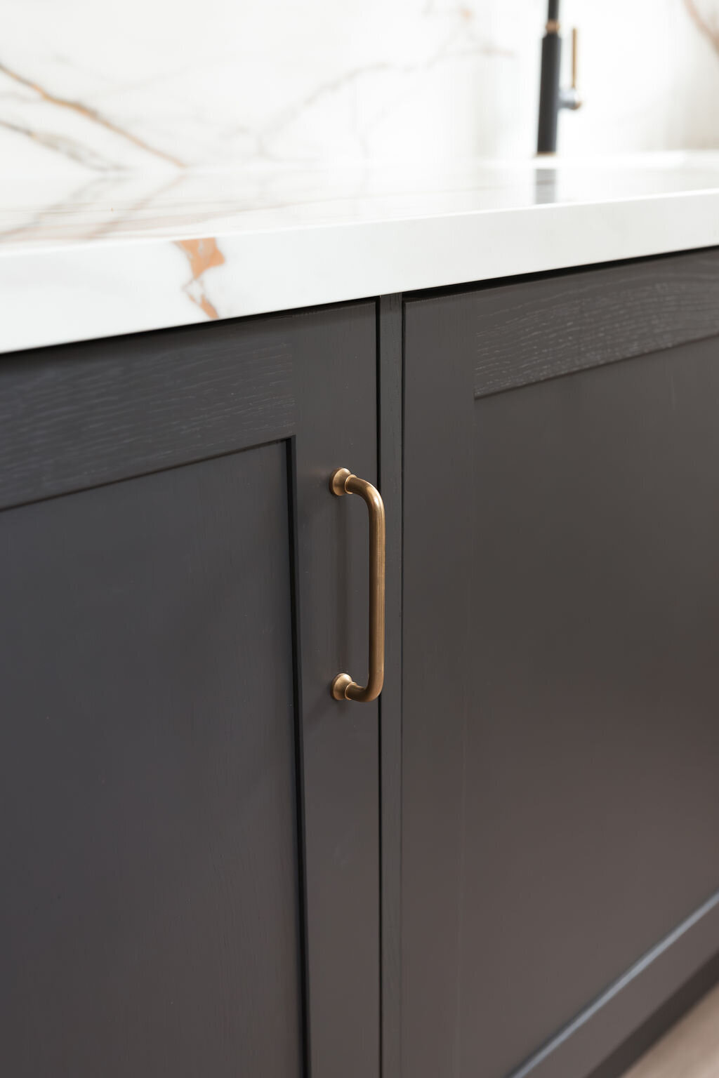 Black lower cabinets with gold handles, below a white marble countertop, veined with black and brown.