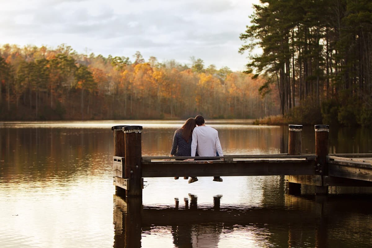 Engagement portrait of a couple sitting on a dock looking out over the water at sunset in Peachtree City Georgia.
