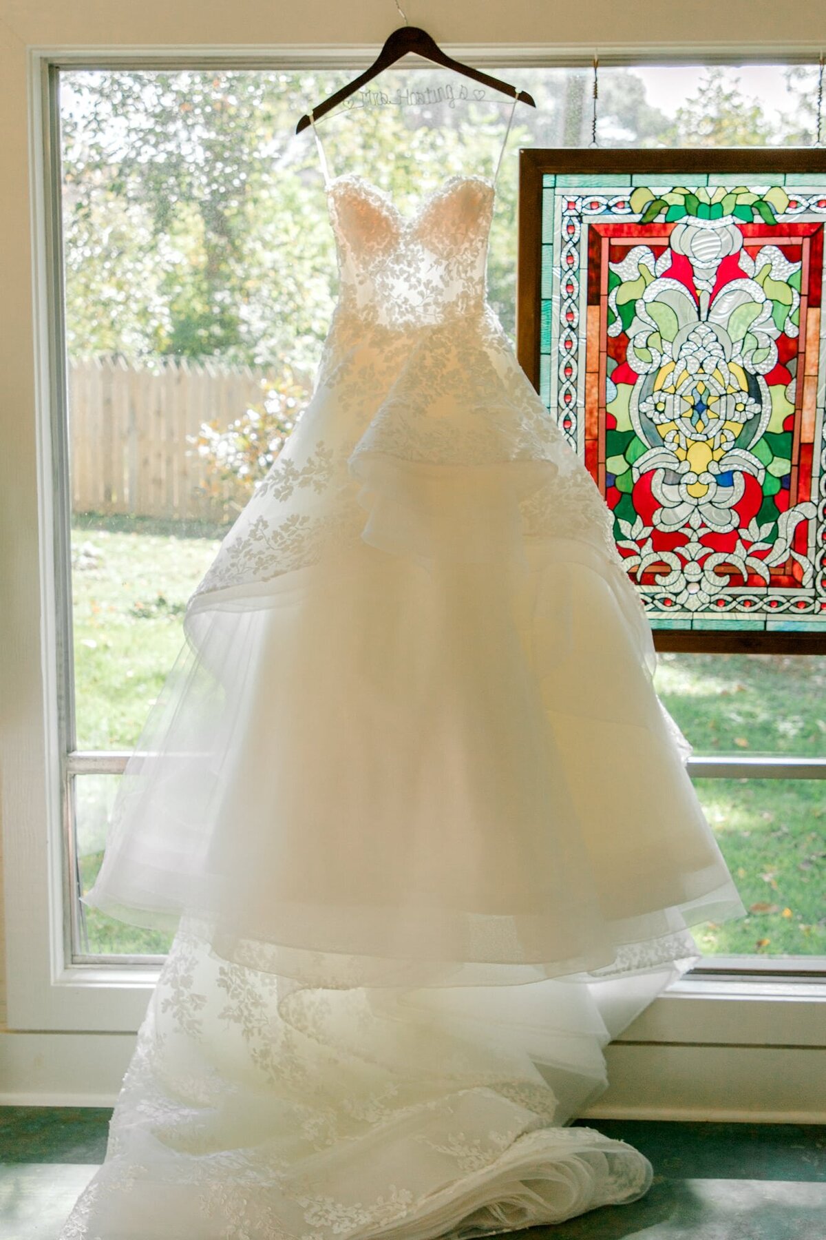 Wedding dress ballgown hanging in front of stained glass frame