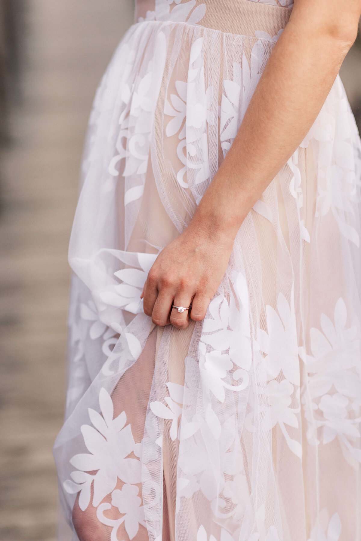 Bride holding her engagement ring against her dress.