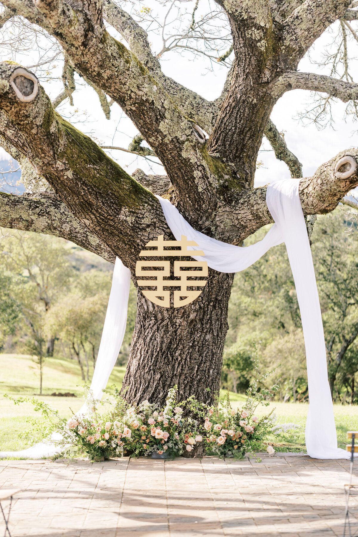 walnut tree at napa wedding ceremony venue with floral grounded arch installation and white linen draping under double happiness sign