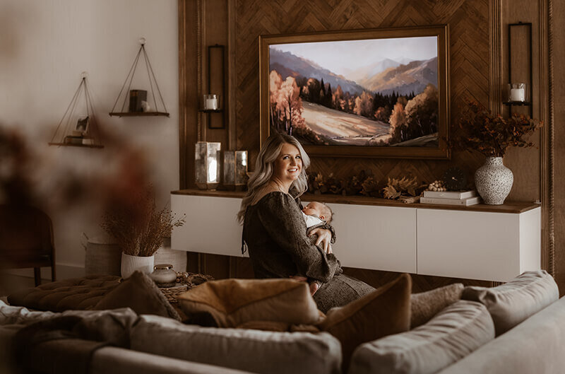 Mom cuddling newborn son while sitting on coffee table in custom designed living room