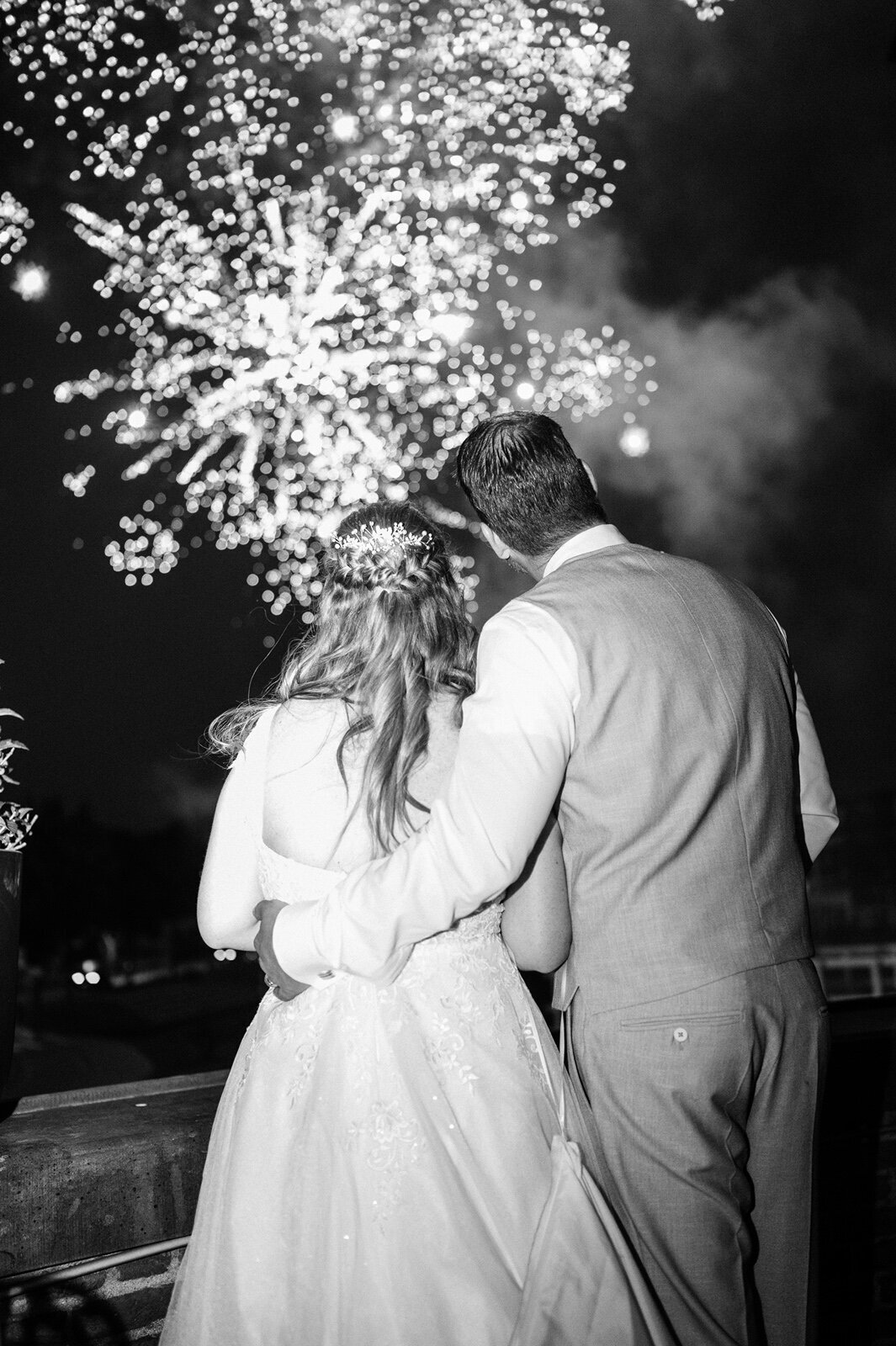 Bruidspaar staat met rug naar trouwfotograaf terwijl ze kijken naar het vuurwerk