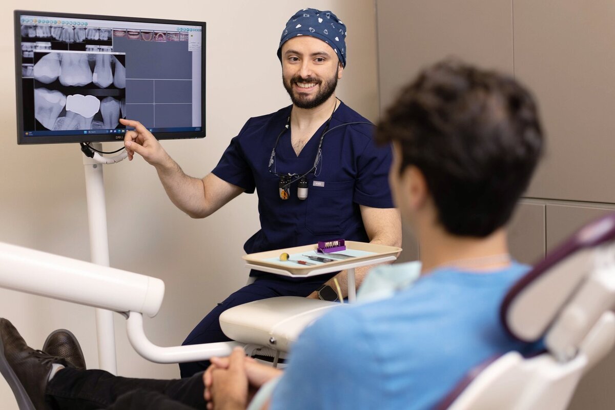 Dentist smiling at patient while pointing to an X-ray