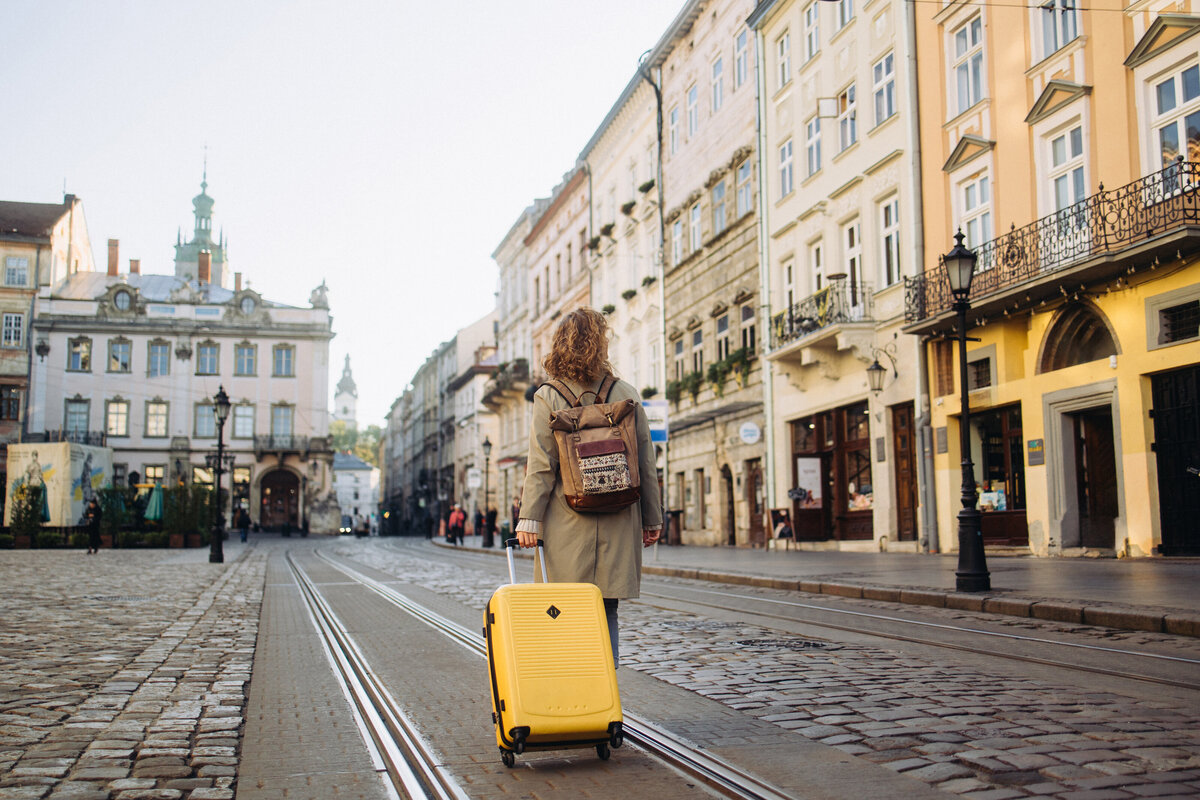 A woman is walking through cobblestone streets of Europe puling a yellow suitcase.